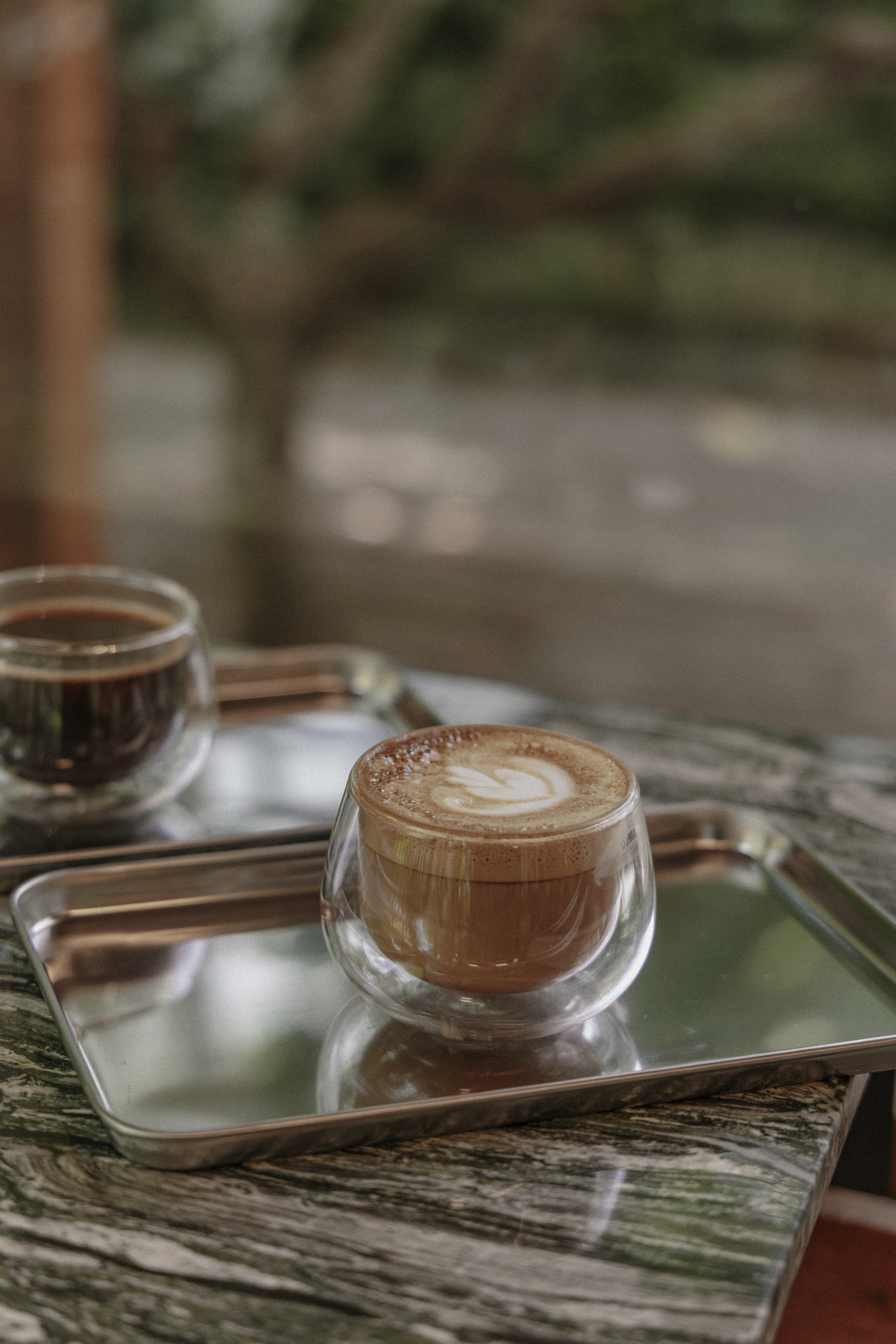 Latte art in glass cup on green marble, garden bokeh background